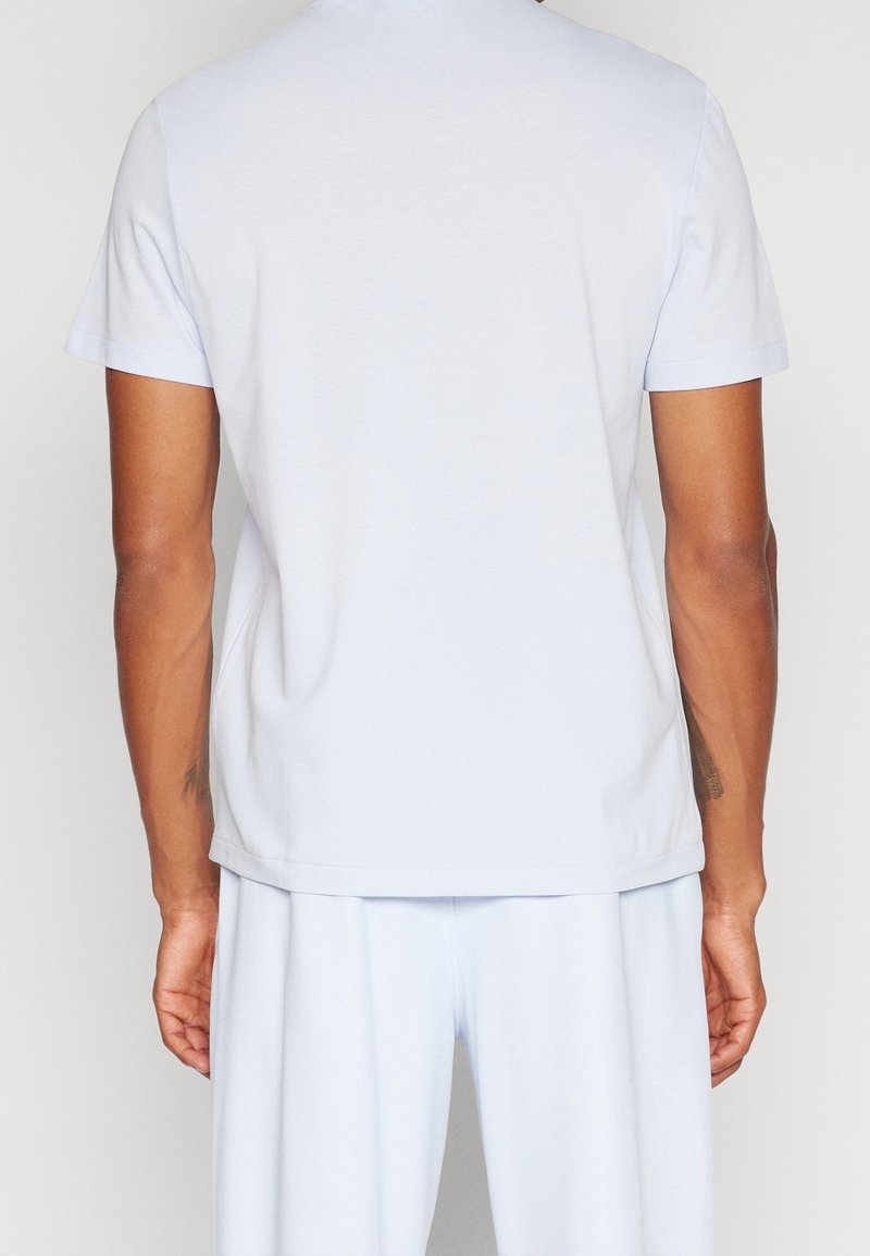 Jasnoniebieska bawełniana koszulka z krótkimi rękawami, okrągłym dekoltem i luźnym krojem. Gładka faktura bez widocznych wzorów czy zdobień.