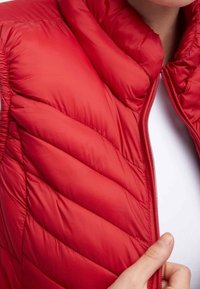 Rood gewatteerd bodywarmer met een hoge kraag, een doorgestikt patroon en een ritssluiting. Gladde textuur met geplooide details bij de schouders.