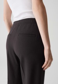 Pantaloni neri su misura con una texture liscia, dotati di una comoda vita elasticizzata e due tasche posteriori discrete.