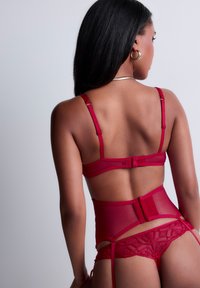 Ensemble de lingerie rouge comprenant un soutien-gorge en mesh transparent avec des bretelles ajustables, une ceinture porte-jarretelles taille haute et un string en dentelle avec des motifs géométriques.