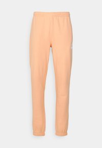 Persikofärgade träningsbyxor med elastisk midja, avsmalnande anklar och sidsömmar. Har en liten vit logotyp på höger ben.