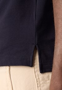 Navy polo shirt van stof met een gestructureerde weving, voorzien van zijsplitten aan de zoom, gecombineerd met lichtbeige chino's met zichtbare stiksels.