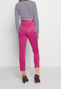 Pantaloni di cotone rosa con gamba dritta, vita alta e tasche frontali, abbinati a una maglietta a righe bianca e nera e scarpe con tacco marroni.