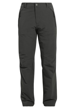 Man loopt en draagt een olijfgroene capuchonjas, lichtgrijs t-shirt, donkergrijze broek en zwarte schoenen tegen een effen achtergrond.