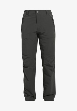Man loopt en draagt een olijfgroene capuchonjas, lichtgrijs t-shirt, donkergrijze broek en zwarte schoenen tegen een effen achtergrond.