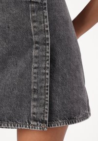 Svart denim mini kjol med fransad fåll, synlig söm och en något A-linjeformad design. Materialet har en bleknad textur.