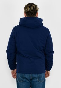 Giacca blu navy con cappuccio, presenta una texture liscia e un design imbottito, che mette in evidenza una silhouette posteriore semplice e funzionale.