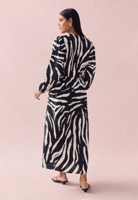 Maxi dress featuring a black and white zebra pattern, with long sleeves, a cinched waist, and lightweight fabric. Styled with black footwear.