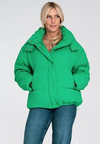 Zielona kurtka puchowa z wysokim kołnierzem, złotymi elementami oraz zapięciem na guziki. Posiada boczne kieszenie i miękką, pikowaną teksturę.