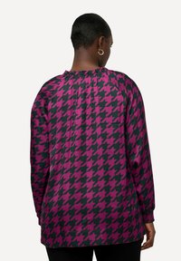 Langærmet bluse med houndstooth-mønster i pink og sort, der har en sammensnørret halsudskæring og elastiske manchetter. Glat stofstruktur.