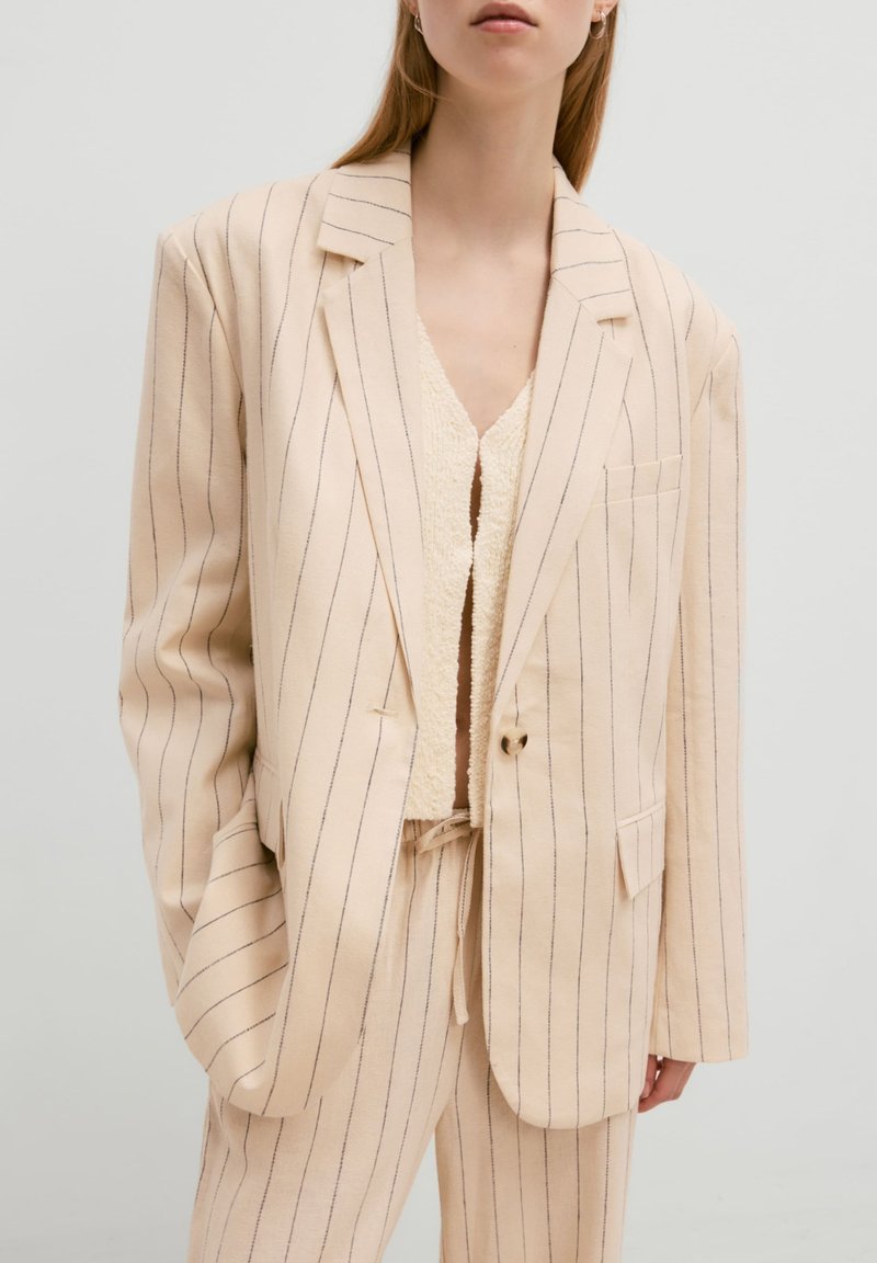 Beige gestreepte blazer met revers en een enkele knoopsluiting, gecombineerd met een textuur crème top en bijpassende broeken.