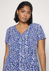 Vestido floral com decote em V, mangas curtas e corpete ajustado com detalhes em botões em tons de azul e branco sobre um fundo azul-marinho.
