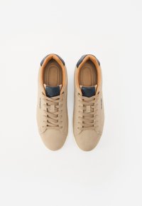 Tan sneakers made of suede with a rounded toe shape, featuring beige laces, a brown inner lining, and a navy blue heel accent.