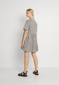 Gestreiftes Kurzarmkleid in Beige und Schwarz, mit einem ausgestellten Rock und einer taillierten Taille. Getragen mit schwarzen Sandalen, die ein lässiges Design zeigen.