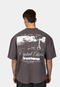 Šedé oversize tričko s černobílou grafikou Eiffelovy věže a textem pod obrázkem "Crystal Paris Champs."