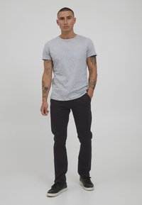 Grå bomullströja med rund halsringning och korta ärmar, i kombination med svarta slim-fit byxor och svarta sneakers med vita sulor.