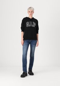 Black hooded sweatshirt with "GAP" logo, paired with blue jeans and black platform shoes. Simple design, casual fit, and solid colors.