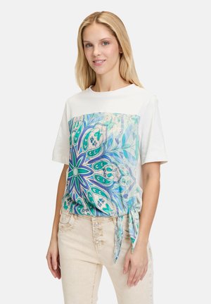 Witte T-shirt met korte mouwen en een kleurrijke, bedrukt voorzijde met blauwe en groene bloemmotieven; inclusief zijriemdetail.