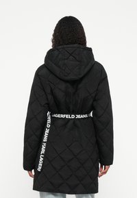 Cappotto imbottito nero con cappuccio, caratterizzato da una vita con cintura e branding "LAGERFELD JEANS", tessuto testurizzato e maniche lunghe.