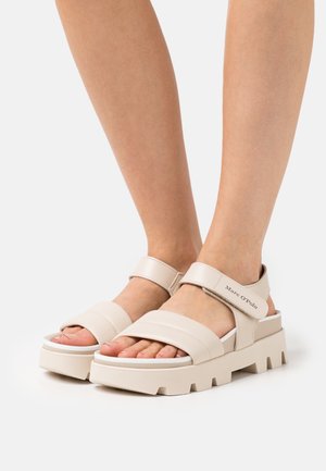 Sandales à plateforme beige avec des larges brides, boucle ajustable et semelle texturée. Nom de la marque visible sur la bride latérale.