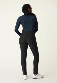 Top blu navy a maniche lunghe con un design aderente abbinato a pantaloni neri a vita alta; l'outfit è completato da scarpe da ginnastica bianche.