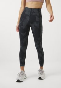 Leggings pretos de cintura alta com um padrão de nuvens subtil, feitos de material elástico. Combinados com sapatilhas cinzentas e uma blusa rosa clara.