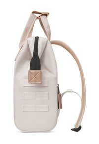 Sac à dos en tissu blanc avec une fermeture éclair noire, des accents beige et un patch texturé. Il présente trois sangles horizontales sur le côté.