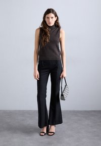 Brown sleeveless turtleneck top, high-waisted black flared pants with button details, and a black-and-white patterned handbag.