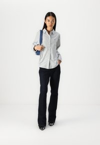 Camicia a righe azzurro chiaro con bottoni, jeans a palazzo blu scuro, scarpe nere con punta e zaino blu; tessuto liscio, vestibilità sartoriale.