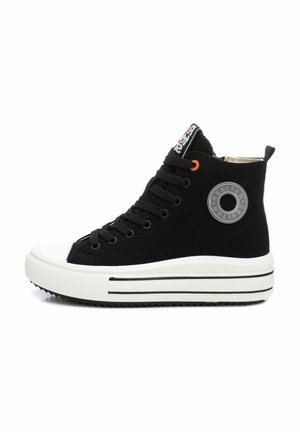 Zapatilla alta negra con suela de goma blanca plana, ojales negros, acento naranja y detalle del logo circular en el lateral.