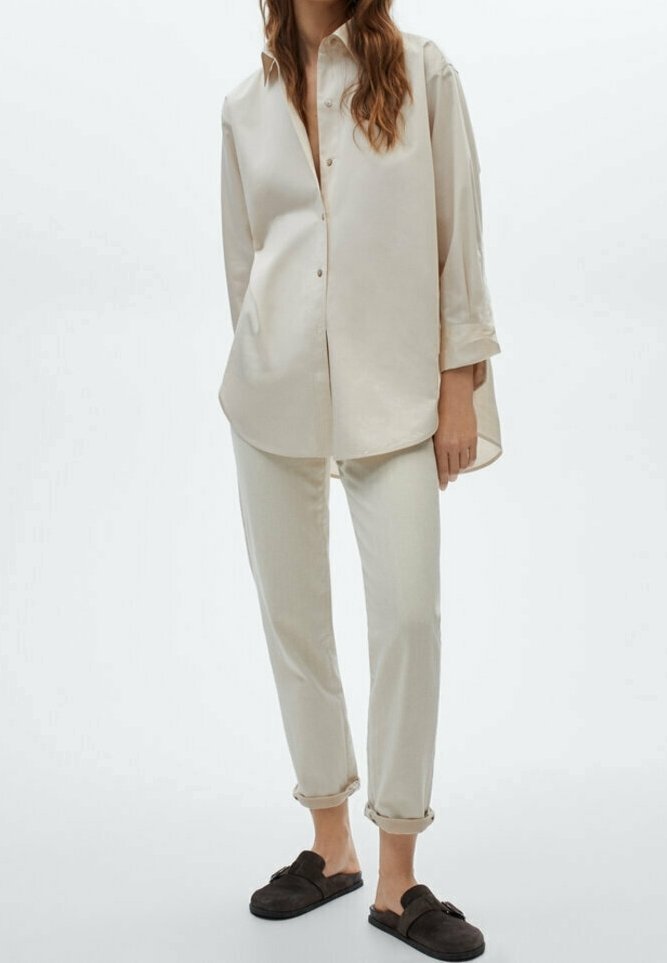 Chemise oversize beige clair avec des boutons, associée à un jean beige clair retroussé et à des mocassins marron foncé. Texture de tissu lisse.