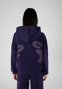 Hoodie viola con un grande motivo grafico in una tonalità più chiara sul retro. Presenta una vestibilità rilassata e un cappuccio con coulisse.