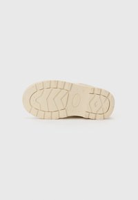 Suela de una zapatilla, con un color beige claro, material de caucho, superficie texturizada con un patrón de relieve en zigzag y bordes redondeados.