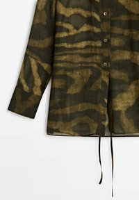 Chemise à manches longues en tissu léger avec imprimé animalier vert et marron, fermeture à boutons et liens latéraux pour un ajustement personnalisé.