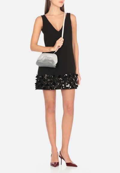 Abito nero senza maniche con scollo a V, caratterizzato da un orlo texturizzato con accenti floreali neri e argento. Abbinato a una pochette argento e tacchi rossi.