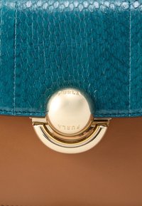 Τσάντα χειρός από δερματίνη σε τυρκουάζ απόχρωση με χρυσαφένια μεταλλικά στοιχεία και στρογγυλό κούμπωμα. Έχει λείο καφέ πάτο και περίτεχνα ραφτά διακοσμητικά στοιχεία.