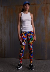 Leggings coloridos com um padrão floral em vermelho, amarelo, verde e azul. Combinados com uma blusa de alças branca e ténis pretos. Fundo escuro.