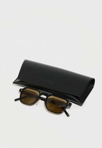 Fekete napszemüveg barna lencsékkel, téglalap alakú kerettel és arany díszítéssel, egy fekete bőrtok mellett elhelyezve.