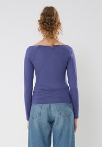 Lilla langermet topp med bred halslinning, glatt tekstur og tettsittende design, kombinert med lyseblå høy midje vide bukser.