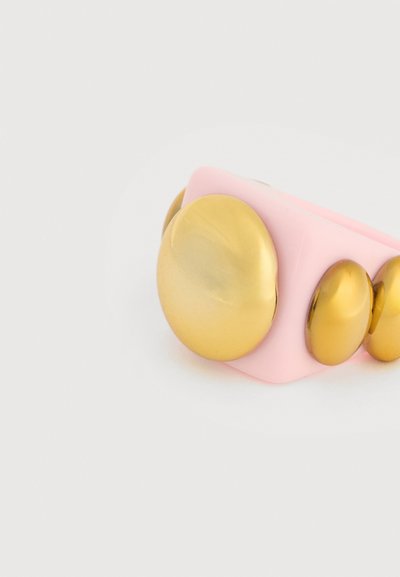 Rosa armbånd med tre store, skinnende, gullfargede sirkulære nagler arrangert i synkende størrelse på en ensfarget bakgrunn.