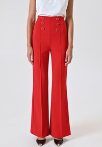 Pantalons évasés rouges en tissu lisse, comprenant une taille haute, un devant boutonné avec des accents circulaires et des détails de plis le long des jambes.