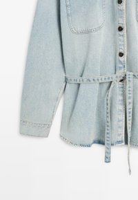 Lichtblauw denim overhemd met lange mouwen, zwarte knopen, borstzak en bijpassende stoffen riem gestrikt in de taille.