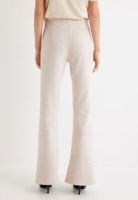 Lichtbeige flared broek van een zachte, gestructureerde stof, met een hoge taille en een aansluitende snit tot aan de knie, eindigend in een vloeiende zoom.