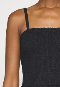 Haut court noir froncé avec fines bretelles. Tissu texturé, corsage élastiqué et coupe ajustée pour un look épuré.