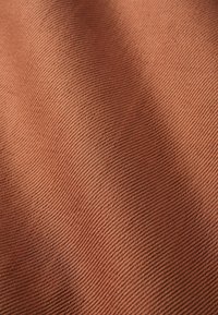 Texturovaná tkanina v teplé hnědé barvě s jemnými diagonálními pruhy, která ukazuje hladký a odolný povrch.