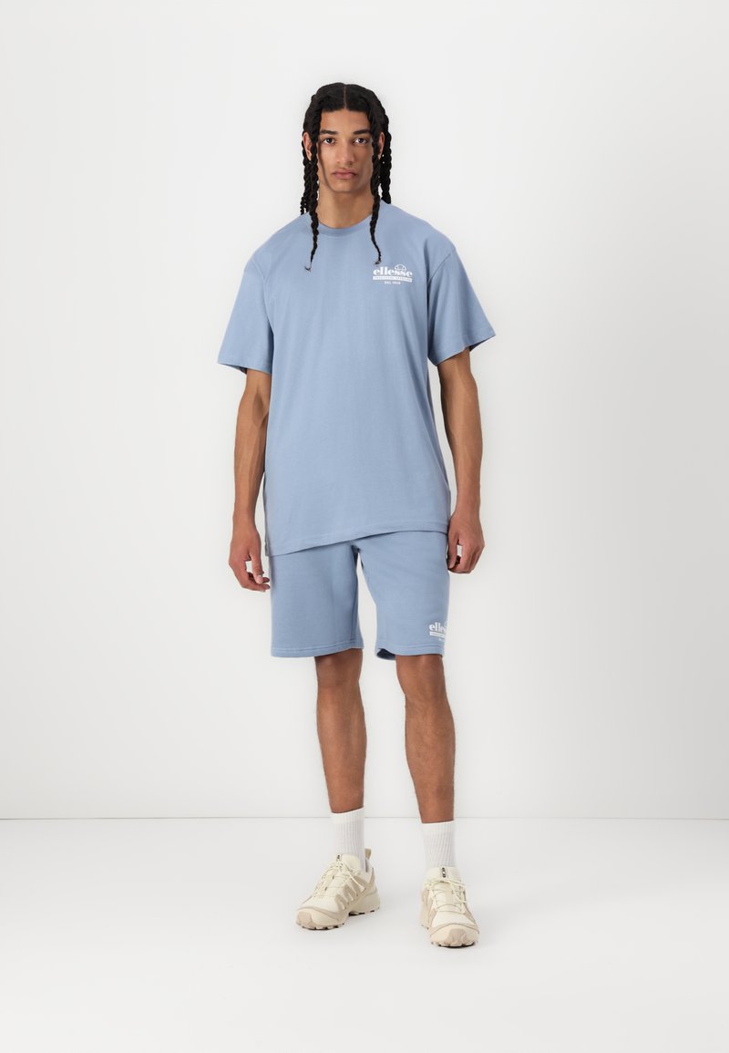 T-shirt in cotone azzurro chiaro e pantaloni corti abbinati. Design semplice con un logo stampato sul petto e sui pantaloni. Abbinamento con scarpe da ginnastica beige.