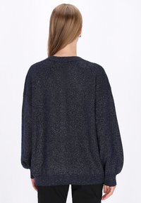 Granatowy sweter o luźnym kroju z metalicznymi drobinkami, z okrągłym dekoltem oraz długimi rękawami z prążkowanymi mankietami i dołem.