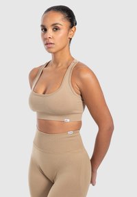 Vaateyhdistelmä beigeistä aktiivivaatteista, johon kuuluu lyhyt urheilurintaliivi leveillä olkaimilla ja korkea vyötärö leggingsit. Sileä tekstuuri, jossa on hienovaraisia brändäysohjeita.