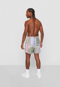 Șorturi de înot cu model patchwork, prezentând motive de batic în nuanțe de verde, albastru și portocalie, cu un brâu elastic și buzunare laterale. Adidași albi și șosete până la glezne.
