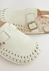 Des chaussures blanches en suède à enfiler, avec un design tressé sur les bords, une sangle avec boucle et une texture naturelle sur la semelle intérieure.